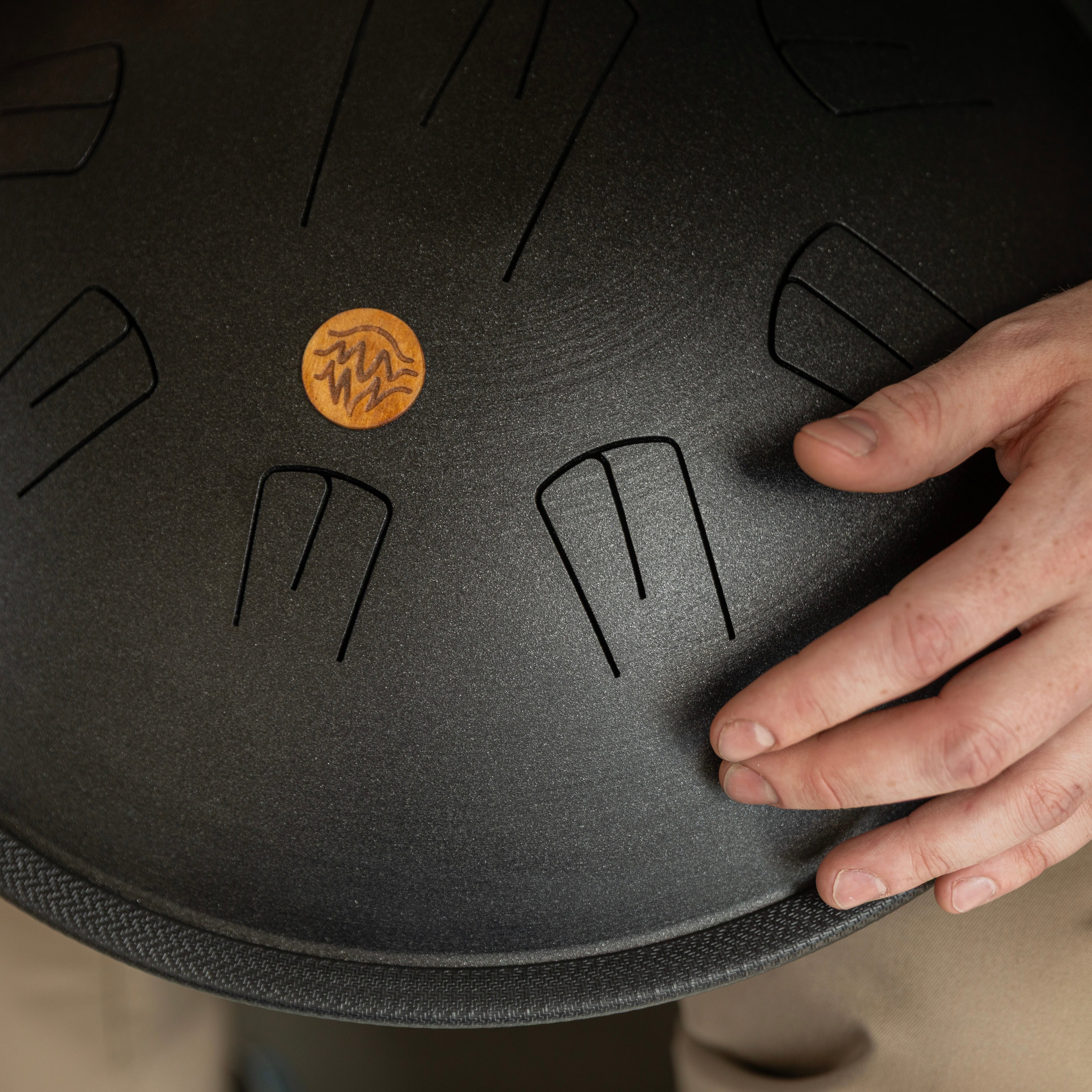 Detailed zoom view how hand holding a black handpan drum with a wooden logo of Burning27